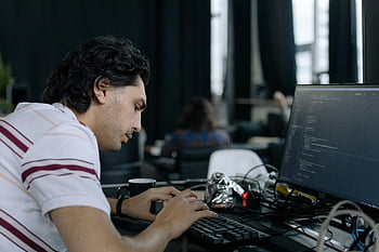 employee working, HTML editor, coder typing, contemporary office, workstation setup, programming code, software development, computer screen, software engineer, intense focus, keyboard typing
