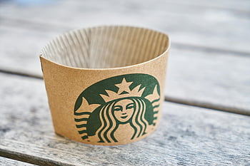 Starbucks, coffee sleeve, eco-friendly design, cardboard sleeve, wooden table, classic coffee setting, brown paper, gray wooden surface, close-up, coffee cup sleeve, sustainable packaging