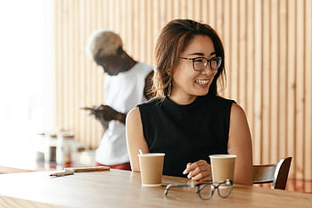 ผู้หญิงเอเชีย, แว่นตา, ที่ยิ้ม, กาแฟ, คาเฟ่สไตล์, เพื่อนร่วมงาน, บทสนทนาที่ผ่อนคลาย, ร่าเริง, ตาราง, ช่วงพักดื่มกาแฟ, การตั้งค่าร้านกาแฟ