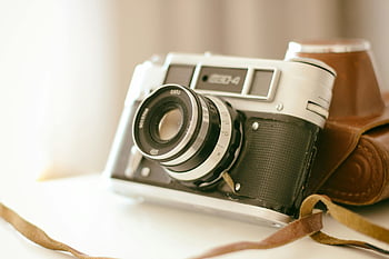 vinobraní fotoaparát, Šedá a černá kamera, kamera pro natáčení, kožené pouzdro, klasický fotoaparát, bílý povrch, kamerové čočky, retro fotoaparát, vinobraní fotografie, popruh fotoaparátu, starožitný fotoaparát