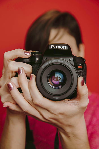 Frau, halten, Schwarze Canon DSLR -Kamera, roter Hintergrund, Foto aufnehmen, Canon EF -Objektiv, Fotografie, Fotograf, dslr, Kamera, Hände