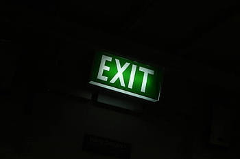exit sign, glowing green, dimly lit, indoor space, emergency exit, safety sign, illuminated sign, building safety, evacuation route, emergency lighting, exit guidance