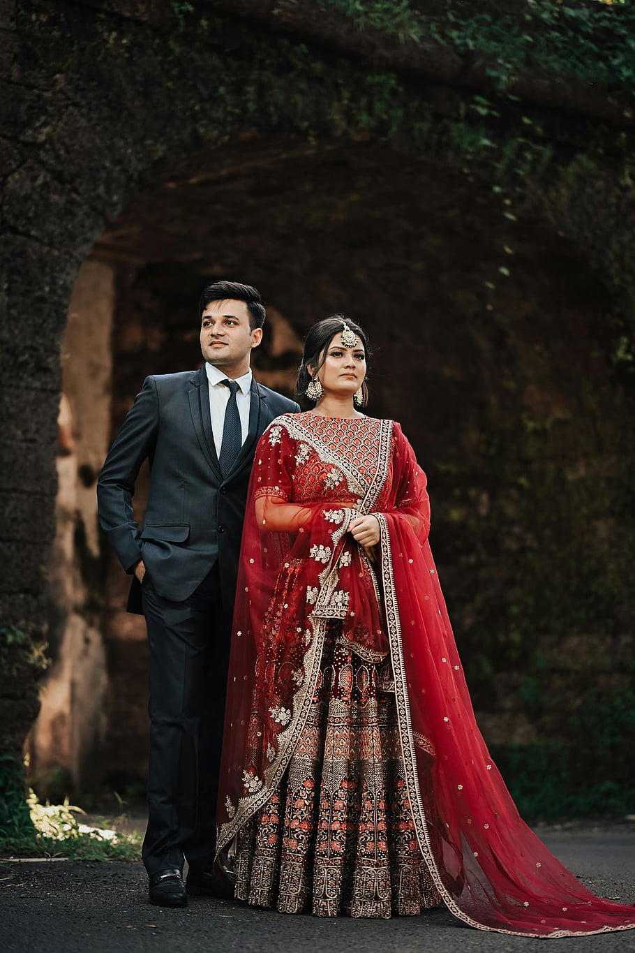 Indian Wedding, couple, traditional attire, outdoor wedding, red lehenga, groom suit, grace, archway, cultural ceremony, romantic scene, heritage celebration