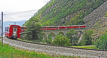 red train, black steel train rail, stone railway bridge, mountainous landscape, lush greenery, picturesque scene, train travel, outdoor scenery, railway tracks, day time, scenic view