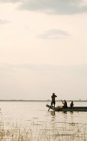 man paddling boat, serene scene, fishermen casting nets, quiet river, sunset, peaceful water, fishing activity, outdoor recreation, natural landscape, calm waters, traditional fishing