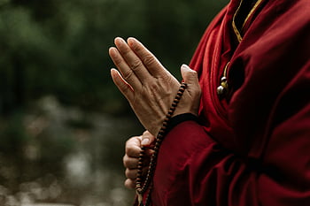 prayer beads, hands holding, brown prayer beads, monk meditating, red robe, outdoor meditation, close-up photo, spiritual practice, meditation beads, religious practice, nature setting
