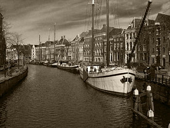 grayscale photography, boats, buildings, sepia-toned image, canal, historical sailboats, classic architecture, waterway, urban scene, vintage boats, old town