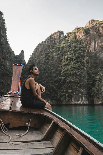 man i svart tank top, brun båt, vattenkropp, kalkstensklippor, klart vatten, krabi, thailand, lugn båttur, man sitter, träbåt, scenisk utsikt
