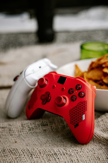 red and white Xbox controllers, wireless controllers, game controllers, textured surface, snacks, background, red controller, white controller, gaming accessories, Xbox accessories, snacks in background