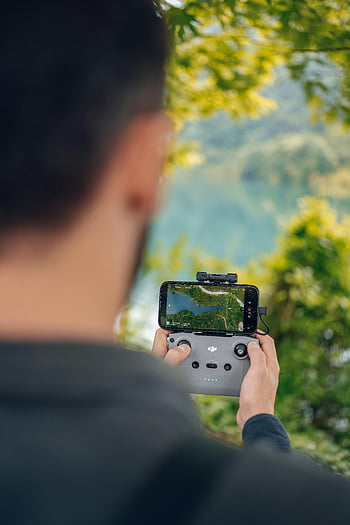 ドローンコントローラー、 ドローンを使う男性、 スマートフォン、 屋外設定、 緑豊かな環境、 テクノロジーに精通した、 ナビゲーション、 ドローン飛行、 リモコン、 緑、 技術