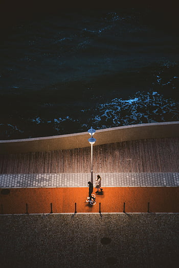 pier at night, couple walking, brightly lit pier, ocean view, night scene, above view, street lamp, waterfront promenade, evening stroll, urban nightlife, waterfront walkway