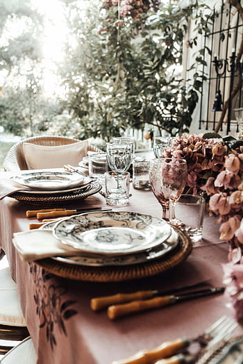 venkovní stolování, banket stůl, Květinové akcenty, Elegantní nádobí, vinné skleničky, Slavnostní příležitost, Sofistikované nastavení, nastavení tabulky, dekorativní květiny, rustikální nádobí, přirozené světlo