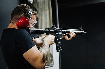 man aiming rifle, indoor shooting range, earmuffs, rifle, shooting, man with tattoos, firearms, indoor range, safety gear, aiming, rifle shooting