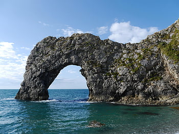 Durdle Door, gray rock formation, body of water, natural rock arch, clear blue sea, sunlight, captivating view, coastal landscape, sea arch, Dorset coast, England
