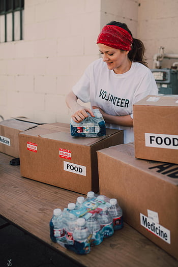 volunteer, packing, food, water, charity, outdoor event, community support, bottles of drinks, brown box, volunteer shirt, food boxes