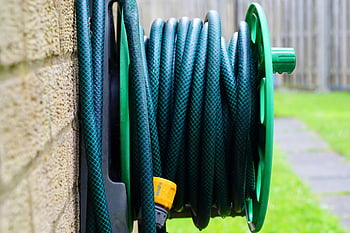 garden hose, wall-mounted reel, brick wall, neatly coiled, outdoor hose, green hose, garden equipment, wall-mounted hose, outdoor storage, garden tools, hose reel