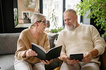 Älteres Paar, Buch lesen, sitzendes Sofa, gemütlicher Innenräume, lächelnd ältere Menschen, entspannendes Paar, Innenumgebung, ältere Menschen, Gemütliches Sofa, Entspannung in Innenräumen