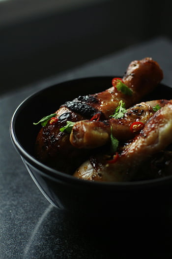 roasted chicken legs, parsley leaves, ceramic bowl, black bowl, close-up, garnished parsley, chili, food photography, chicken dish, savory meal, dark background
