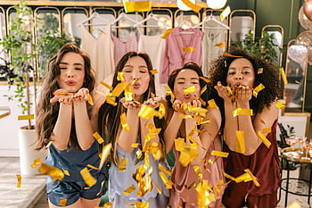 Femmes soufflant des confettis, atmosphère festive, célébration intérieure, confettis en or, célébration joyeuse, quatre femmes, scène de fête, fête des confettis, moment de fête, Femmes célébrant, scène intérieure festive