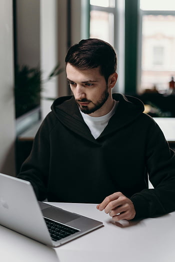uomo nella felpa con cappuccio nero, Usando MacBook, Giovane focalizzato, il computer portatile, scrivania, Elegante ufficio a casa, lavoro, interno, Lavoro casuale, tecnologia, produttività