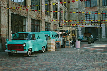 kyiv, Barevné nákladní vozy, živé nádvoří, Urban Street Life, Kulinářská rozmanitost, Zelený minivan, hnědá dřevěná bedna, Hnědý potravinářský vůz, cihlová budova, slavnostní dekorace
