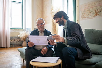 bärtiger Mann, Couch, älterer Kunde, lässiges Büro, Dokumente erörtern, lächelt, Berufstreffen, älterer Mann, jüngerer Mann, Bequeme Einstellung, Freundliche Interaktion