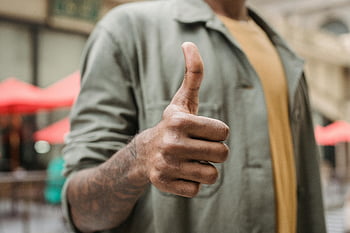 thumbs up, confident man, tattooed arm, outdoor urban area, street scene, positive gesture, casual clothing, urban setting, public space, hand gesture, street photography