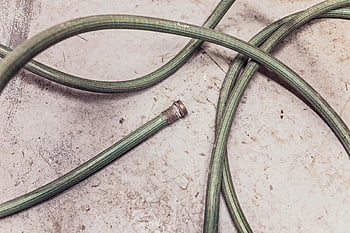 green garden hose, coiled hose, textured concrete, pavement, outdoor hose, garden equipment, outdoor tools, hose on ground, garden hose, concrete surface, hose coiled
