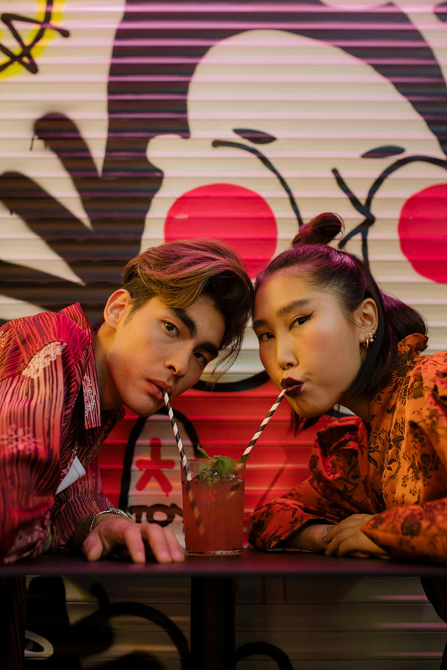 ple drinking, young couple, sharing drink, straws, stylish café, modern graffiti art, colorful drink, urban art, trendy couple, café setting, vibrant colors