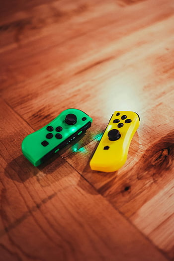 game controllers, green controllers, yellow controllers, hardwood floor, warm lighting, gaming controllers, remote controllers, game console, floor, multi-colored controllers, indoor setting