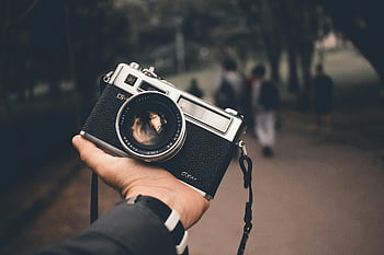 Vintage analogt kamera, Håndholdningskamera, Sort sølvkamera, nærbillede foto, sløret baggrund, mennesker i baggrunden, analog fotografering, vintage kamera, udendørs scene, kamerastropp, Analoge kamerataljer