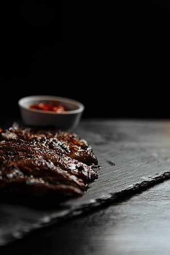 grilled steak, gray stone surface, low-light, moody setting, indulgent meat, grilled meat, side sauce, dark background, steak presentation, food photography, gourmet dish