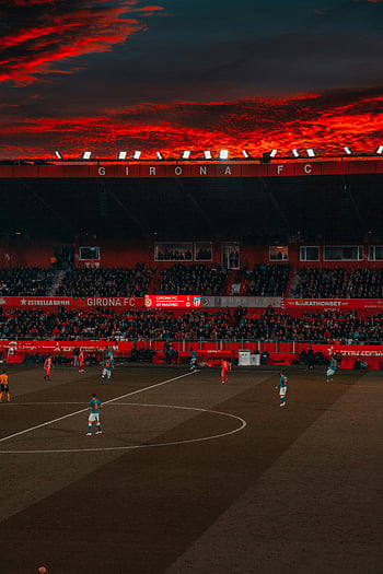 ποδοσφαιρικός αγώνας, Γήπεδο Girona FC, Ζωντανό κόκκινο ουρανό, βραδινό παιχνίδι, έντονο παιχνίδι, ποδοσφαιριστές, δραματικό ουρανό, αθλητικό γεγονός, ποδοσφαιρικό αγώνα, τα φώτα του σταδίου, γήπεδο ποδοσφαίρου