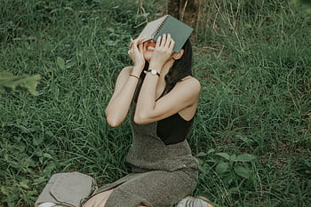 žena čtení, černá tílko, šedé kalhoty, sedí na trávě, slunečný den, venkovní čtení, Mladá žena, rezervovat, travnaté hřiště, Neformální outfit, Nastavení přírody