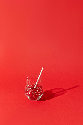 red dice, drinking glass, vibrant red background, still life scene, straw in glass, creative composition, minimalistic setup, striking contrast, red objects, playful still life, artistic arrangement