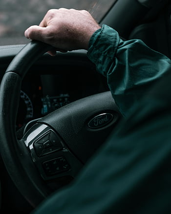 Ford steering wheel, green long sleeve shirt, car interior, dashboard view, hand on steering wheel, Ford vehicle, close-up photo, driving car, car dashboard, steering wheel controls, vehicle interior