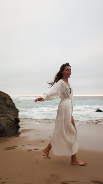 woman in white dress, beach walk, sandy beach, dusk, peaceful walk, ocean waves, barefoot, coastal scene, evening beach, woman enjoying beach, white dress on beach