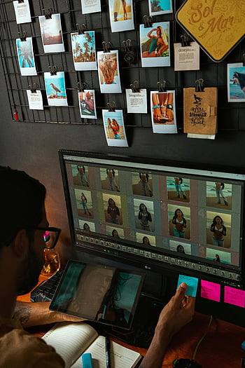 man viewing pictures, computer screen, dual monitors, photo editing, modern workspace, organized workspace, displayed photographs, photo editing software, digital tablet, sticky notes, workspace organization