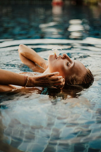 woman in pool, flower on mouth, peaceful floating, Bali swimming pool, eyes closed, serene moment, water relaxation, floral decoration, tranquil scene, poolside beauty, aquatic tranquility
