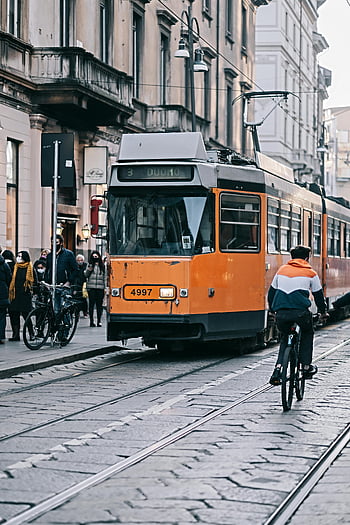 people walking, sidewalk, tram, cyclist, busy street, Milan, Italy, orange tram, urban scene, city life, public transportation