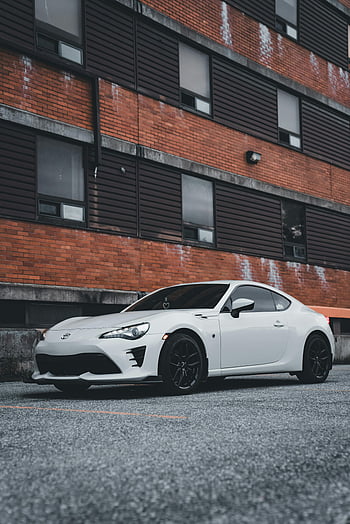 white Toyota 86, residential courtyard, modern apartment block, urban city setting, sleek white car, parked car, Toyota sports car, urban parking, residential parking, modern architecture, cityscape background