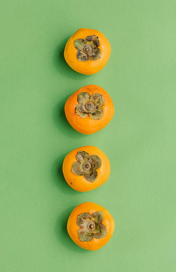 persimmons, green background, fresh persimmons, vibrant green, top view, four persimmons, arranged persimmons, orange fruit, fruit photography, food photography, still life
