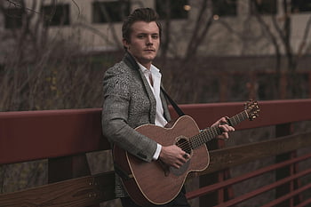 man playing guitar, acoustic guitar, stylish outfit, bridge, handrail, musician, outdoor performance, casual music, urban setting, artistic portrait, musical talent