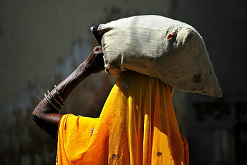 black woman, heavy bag, yellow dress, rural setting, bright sunlight, unrecognizable woman, carrying sack, traditional attire, outdoor scene, cultural image, daily life