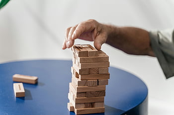 hand building tower, wooden blocks, Jenga blocks, blue table, indoor game, stacking blocks, close-up shot, indoor activity, wooden tower, hand stacking, indoor play
