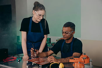 uomo e donna, controllo della scheda madre, assemblaggio di circuiti stampati, spazio di lavoro tecnico, due ingegneri, collaborare, occhiali di sicurezza, banco di lavoro, componenti elettronici, equipaggiamento tecnico, Strumenti dell'area di lavoro