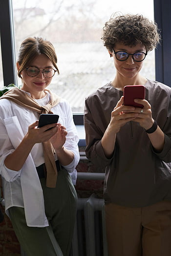 Akıllı telefonları kullanan kişiler, Rasgele Giyinmiş İnsanlar, iç mekan ayarı, insanlar gülümsüyor, akıllı telefonlar, iki insan, rahat kıyafetler, kapalı ortam, Teknoloji Kullanımı, sosyal etkileşim, modern yaşam tarzı