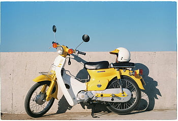 Honda Super Cub, moto amarela, moto vintage, capacete, parede de concreto, céu azul claro, cena ao ar livre, Scooter clássico, bicicleta retro, dia ensolarado, scooter amarelo