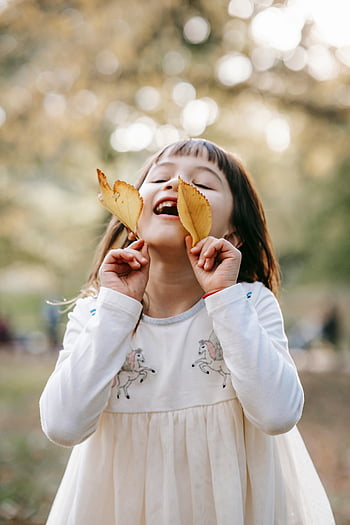 Šťastná holčička, žluté listy, podzimní park, potěšené dítě, hraní s listy, slunečný park, podzim, venkovní zábava, radost z dětství, příroda hrát, podzimní krajina