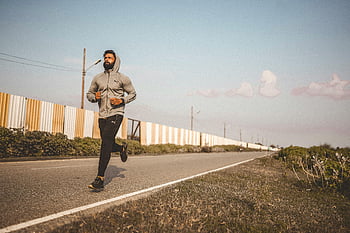 uomo che fa jogging, jogging all'aperto, uomo barbuto, felpa con cappuccio, strada vuota, cielo sereno, uomo che corre, esercizio all'aperto, fitness, uno stile di vita sano, corsa su strada